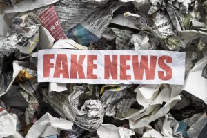 Pila de diaris arrugats amb el missatge “FAKE NEWS” en lletres vermelles destacades, representant la saturació d’informació falsa als mitjans.